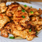 Grilled chicken thighs garnished with chopped green onions on a white plate.