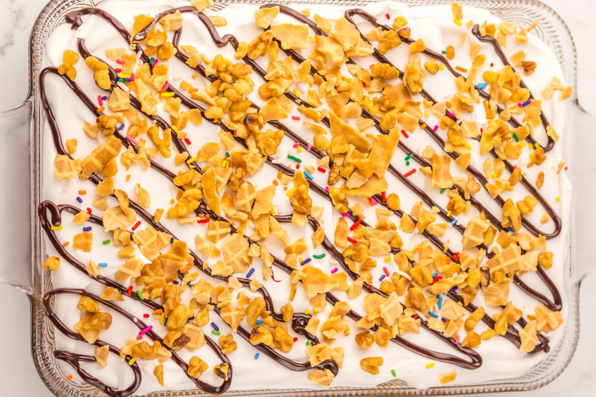 An ice cream cake topped with chocolate drizzle, sprinkles, and waffle cone pieces.