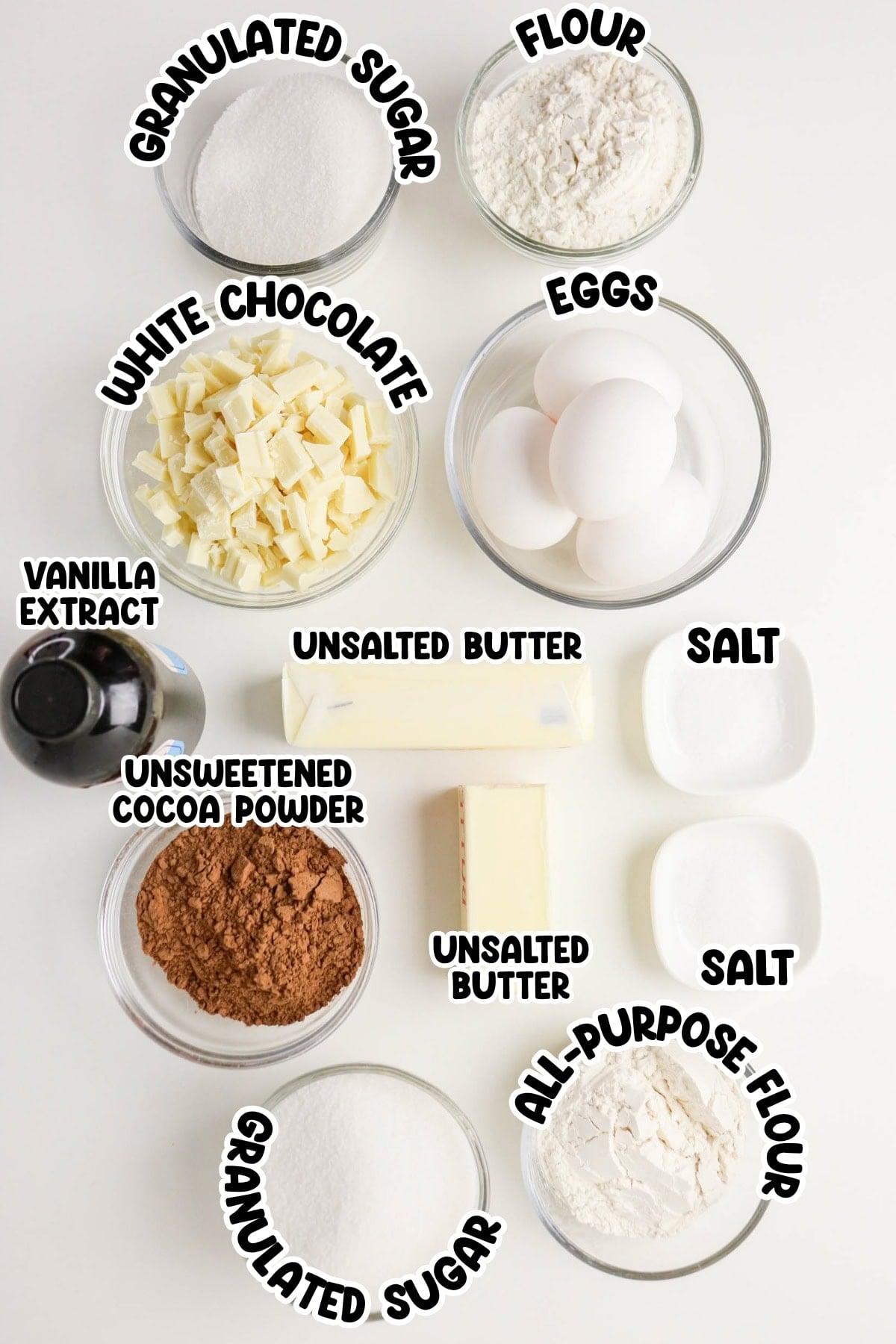 Baking ingredients in bowls: sugar, flour, eggs, butter, cocoa, white chocolate.