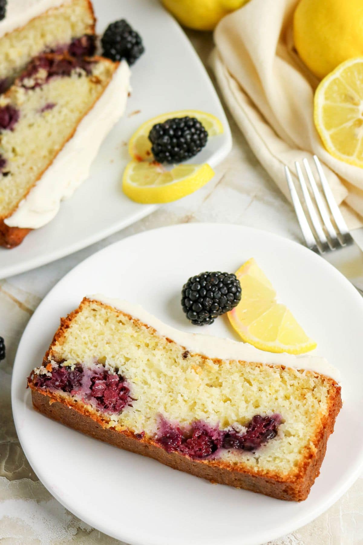 A slice of lemon blackberry bread with icing, blackberries, and lemon slices.
