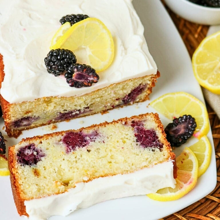 Lemon loaf cake with blackberries, frosting, and lemon slices on top.