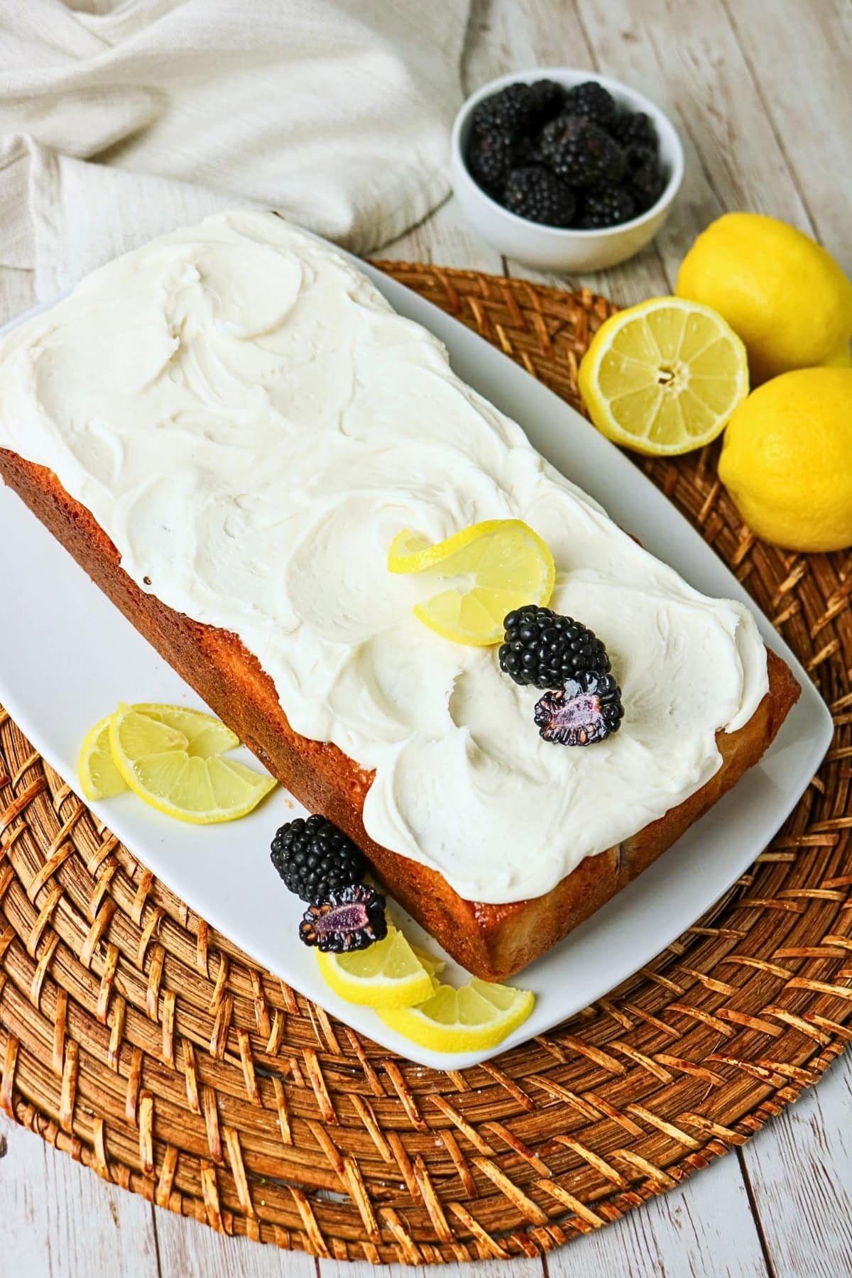Iced loaf cake topped with lemon slices and blackberries on a white platter.
