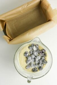 A bowl of batter with floured berries beside a parchment-lined loaf pan.