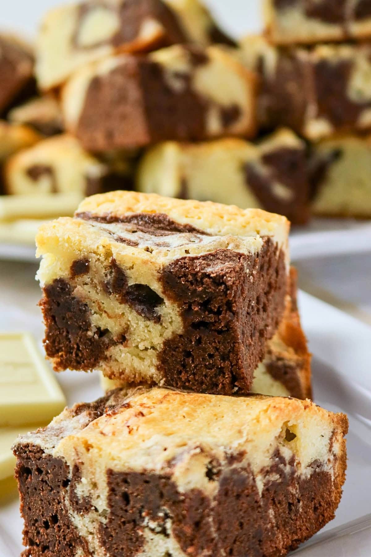 Stacked chocolate and vanilla marbled brownies on a white plate.