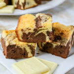 Three stacked marble brownies with white chocolate pieces on a white plate.
