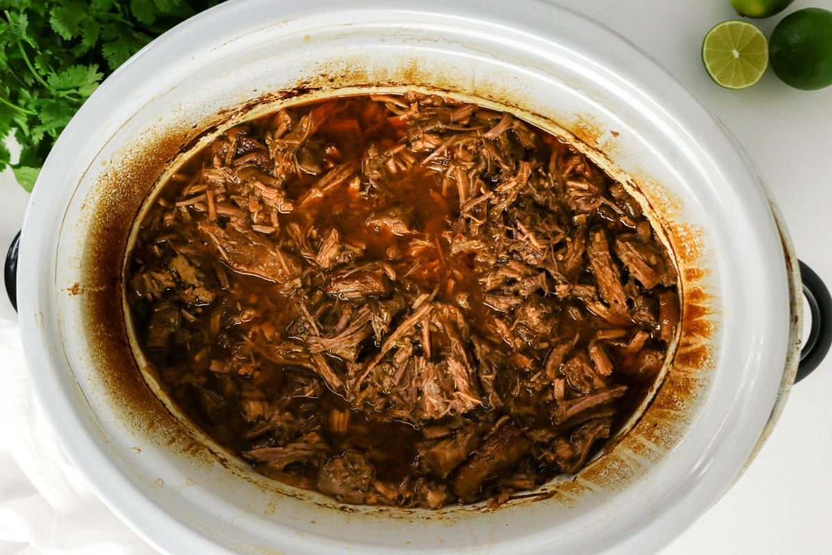 Shredded beef in a slow cooker with rich, dark sauce.
