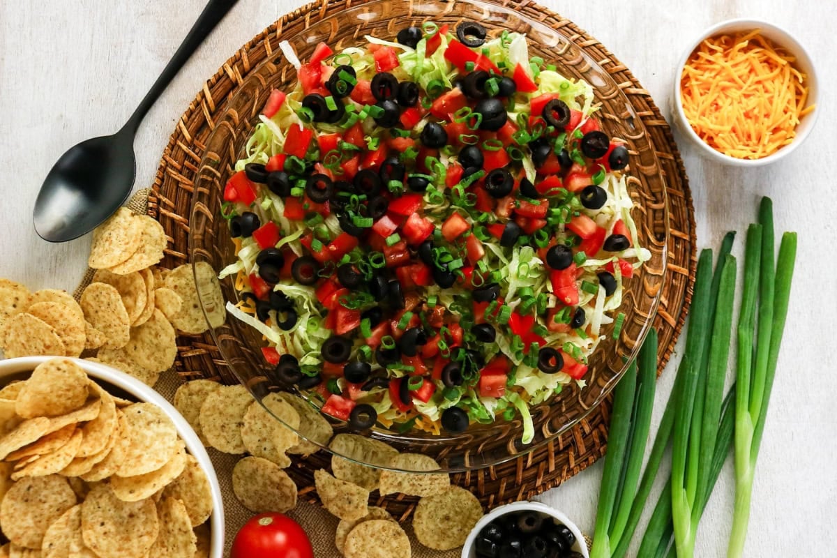 Layered taco dip with tomatoes, olives, green onions, and chips on the side.