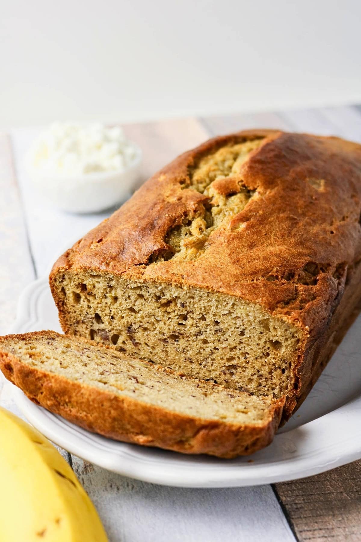 A sliced loaf of banana bread on a white plate, with a bowl of cottage cheese.