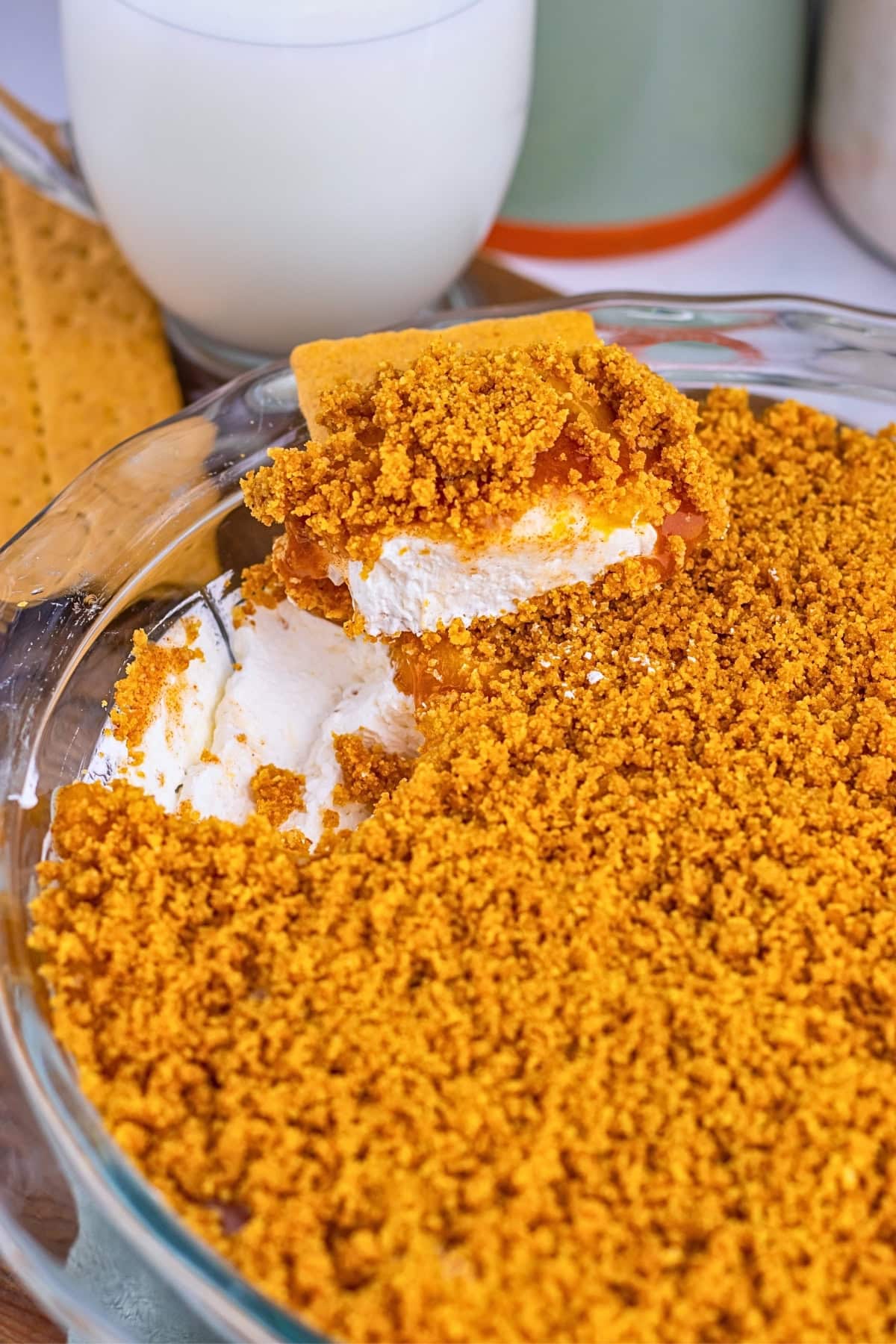 A dessert with a crumbly topping and whipped layer in a glass dish, next to milk.