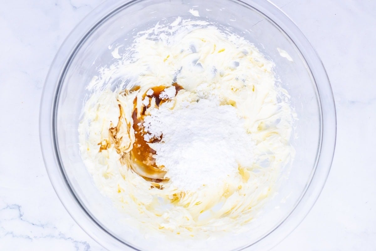 A glass bowl with cream, vanilla, and powdered sugar being mixed together.
