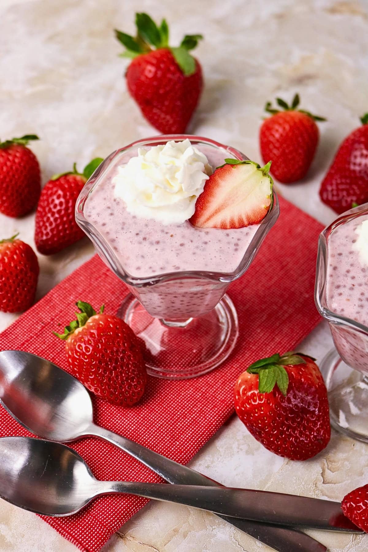 Strawberry chia pudding in glass cups, topped with cream and fresh strawberries.