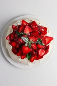 Pavlova topped with fresh strawberries, mint leaves, and powdered sugar.