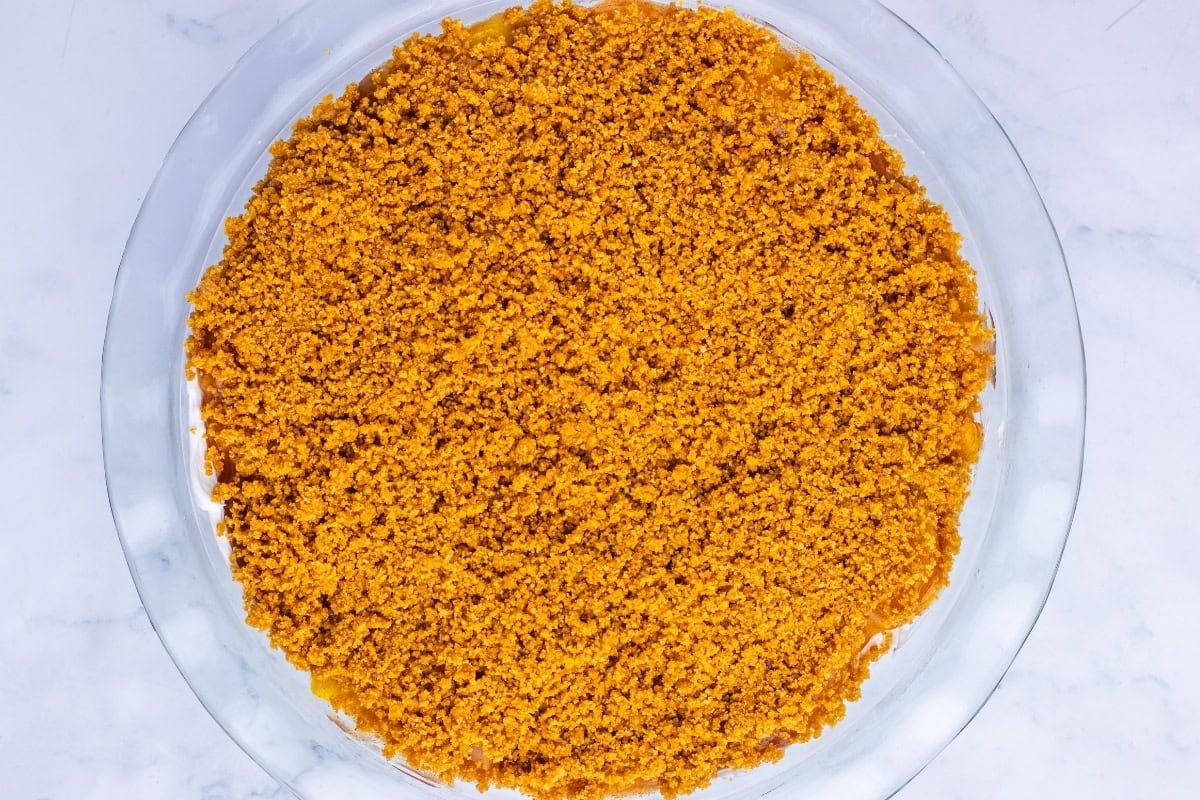 A glass pie dish filled with a layer of golden brown crumb crust.