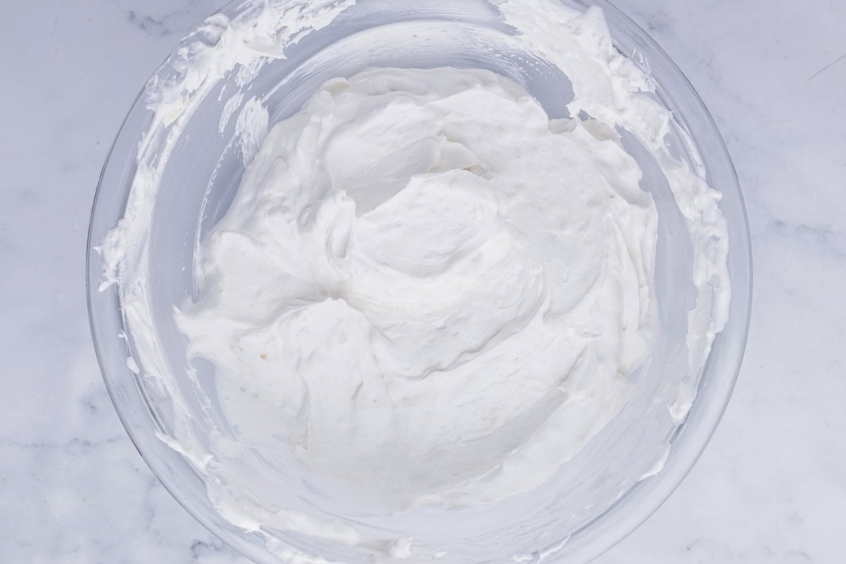 A glass bowl filled with fluffy, white whipped cream on a marble surface.