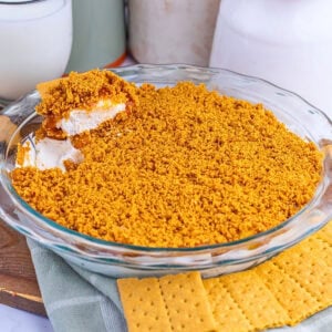 A glass pie dish with a crumbly dessert and a few pieces of graham crackers.