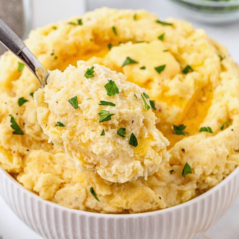 A bowl of mashed potatoes topped with butter and chopped parsley.