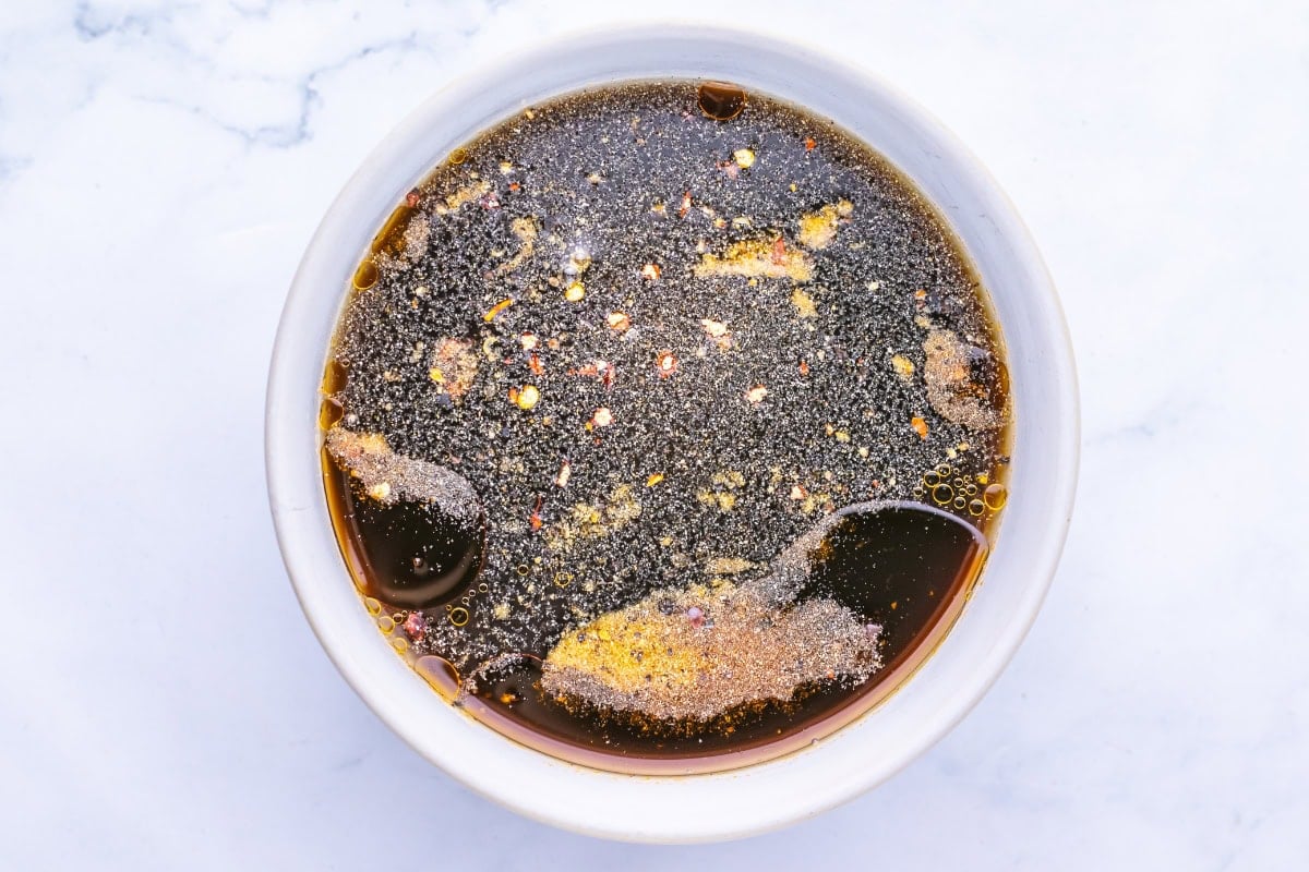 Bowl of dark marinade with spices and oil on a white surface.