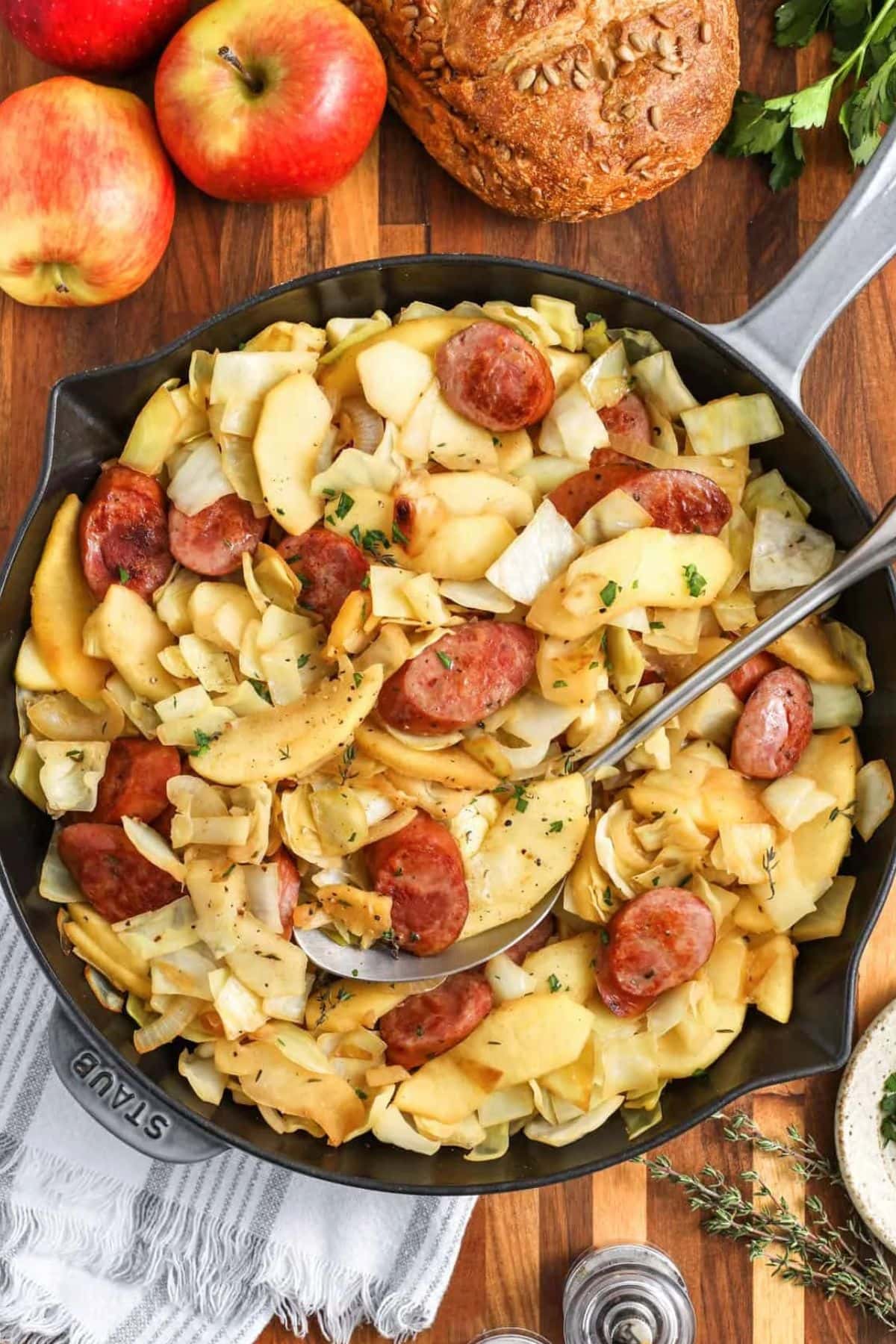 Skillet with sausage, apples, and cabbage, with bread and apples on the side.