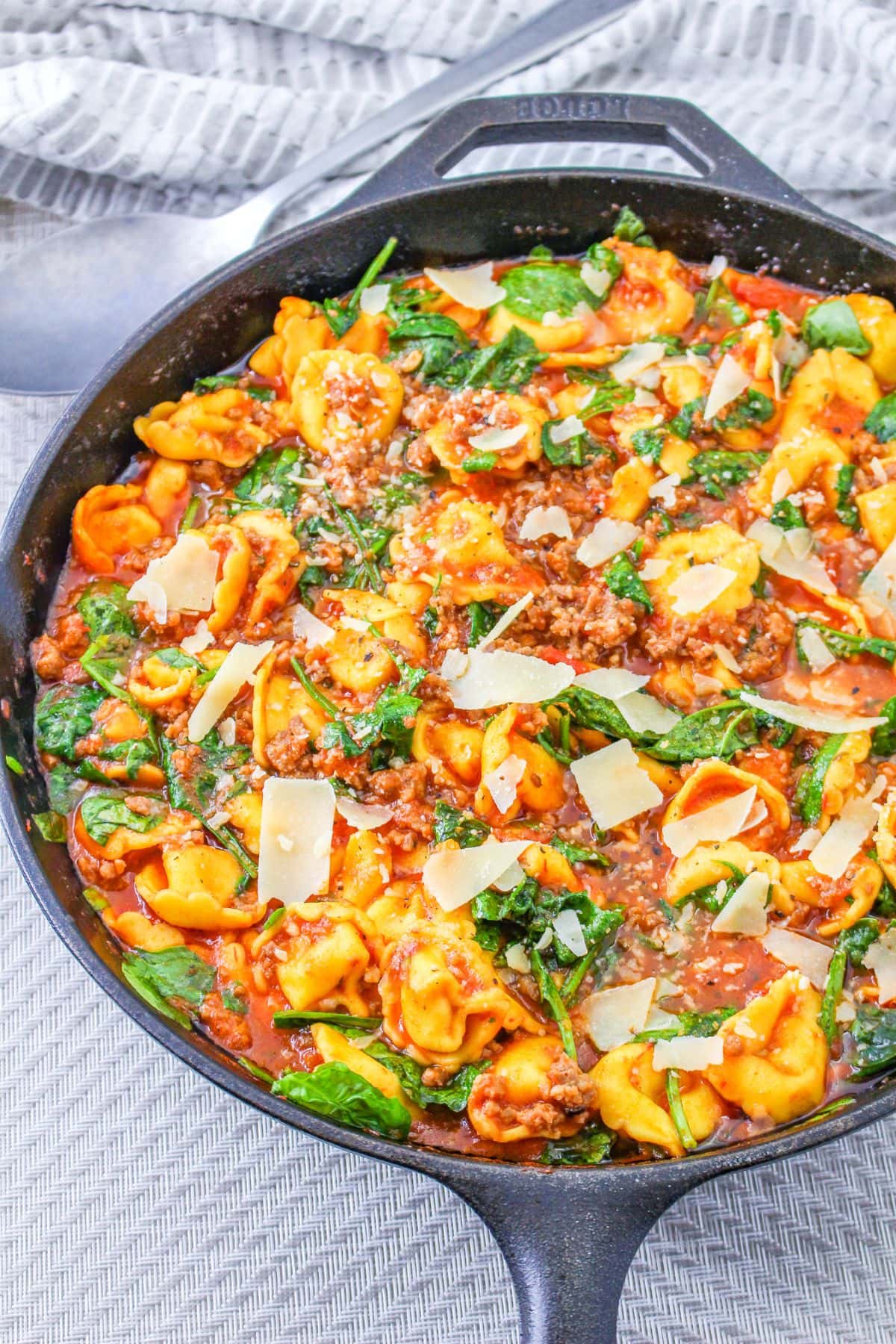 Cheese tortellini with spinach, meat sauce, and parmesan in a black skillet.