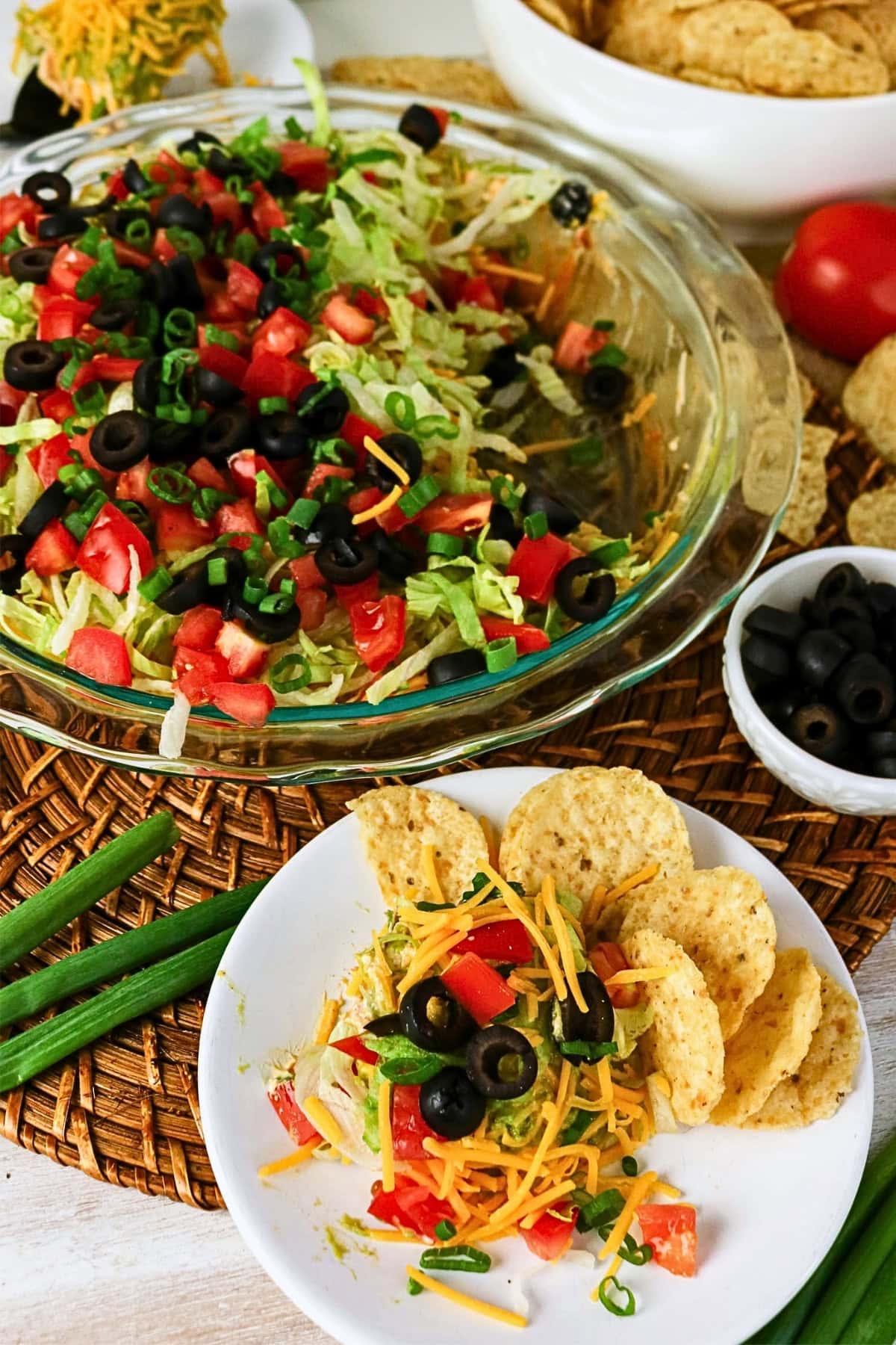 A plate of taco dip with tortilla chips, topped with veggies, cheese, and olives.