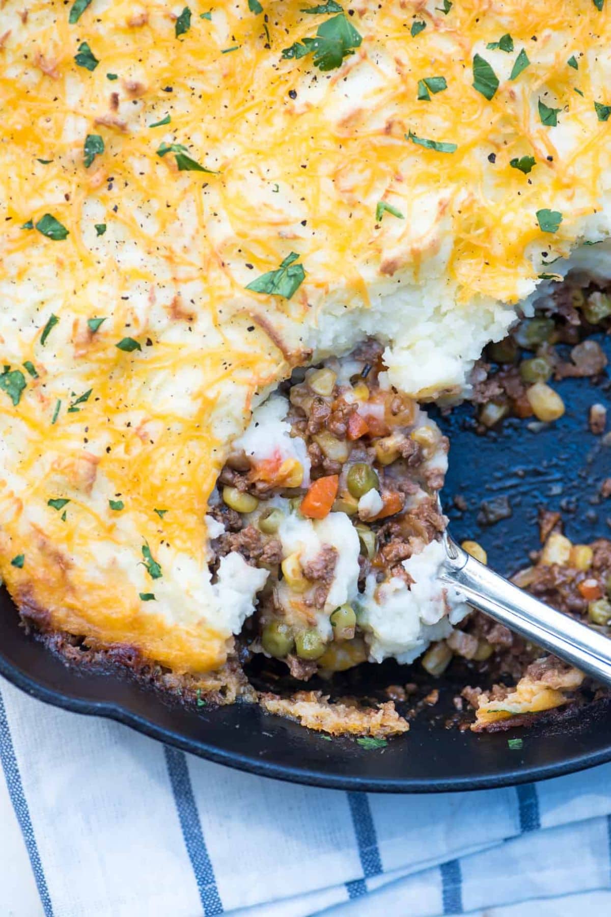 Shepherds pie in a skillet with a serving spoon showing meat and vegetable filling.