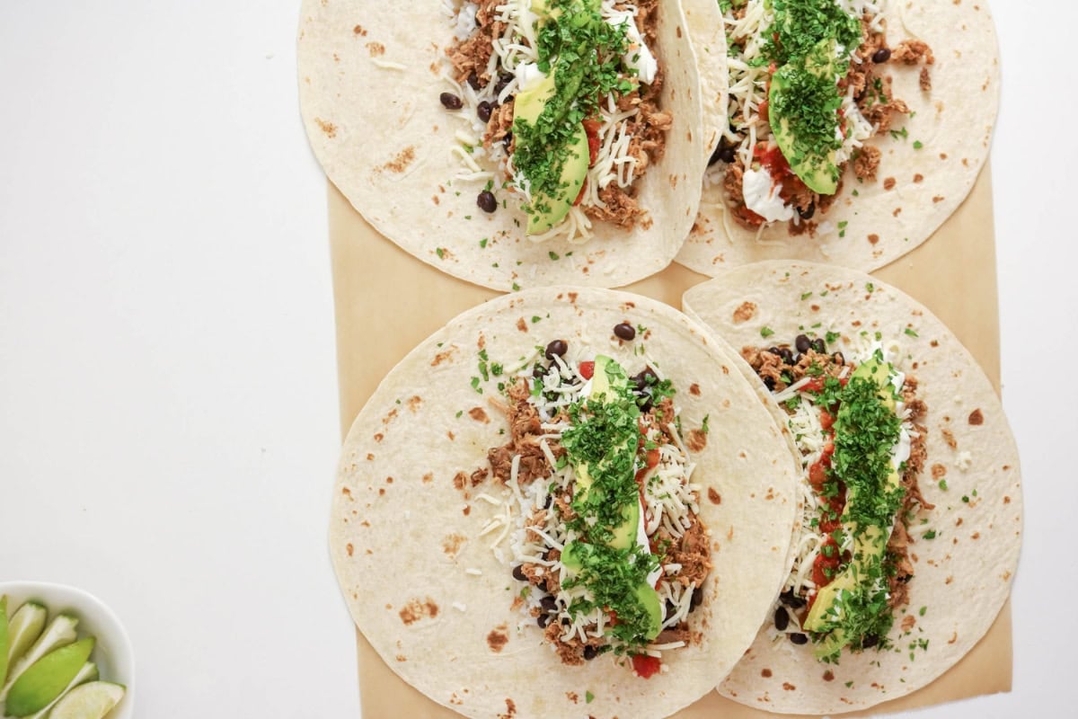 Four open burritos with meat, cheese, beans, sour cream, and green sauce.