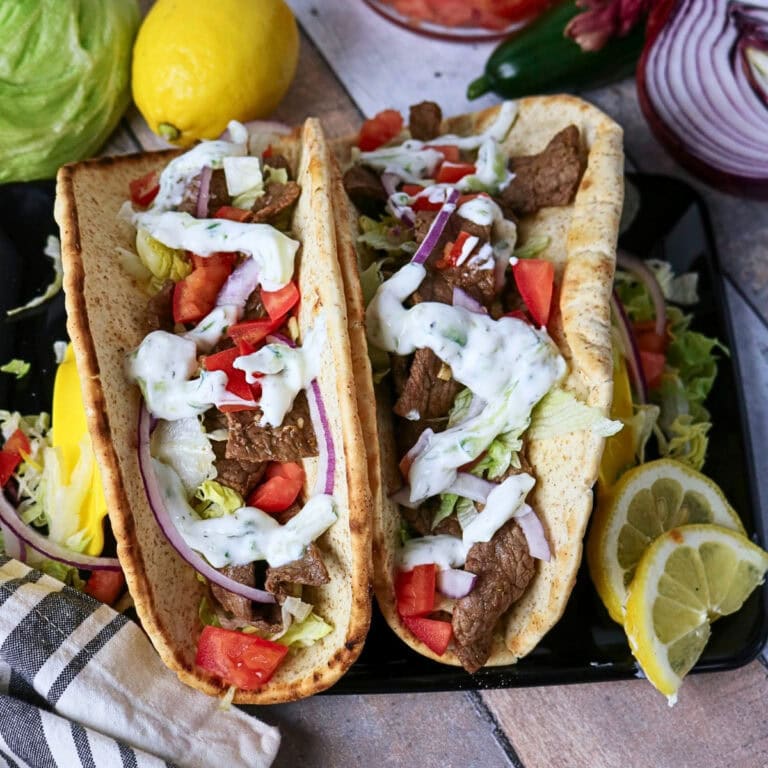 Two beef gyros with lettuce, tomato, onion, and tzatziki sauce on flatbread.