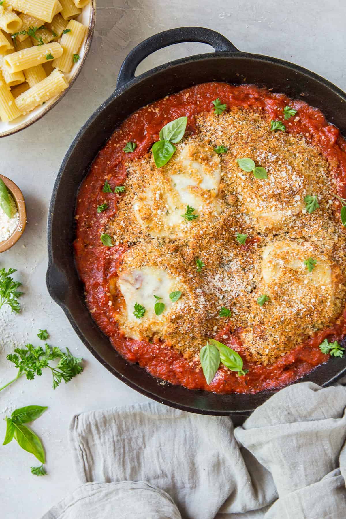 Skillet with breaded chicken in tomato sauce, topped with cheese and herbs.