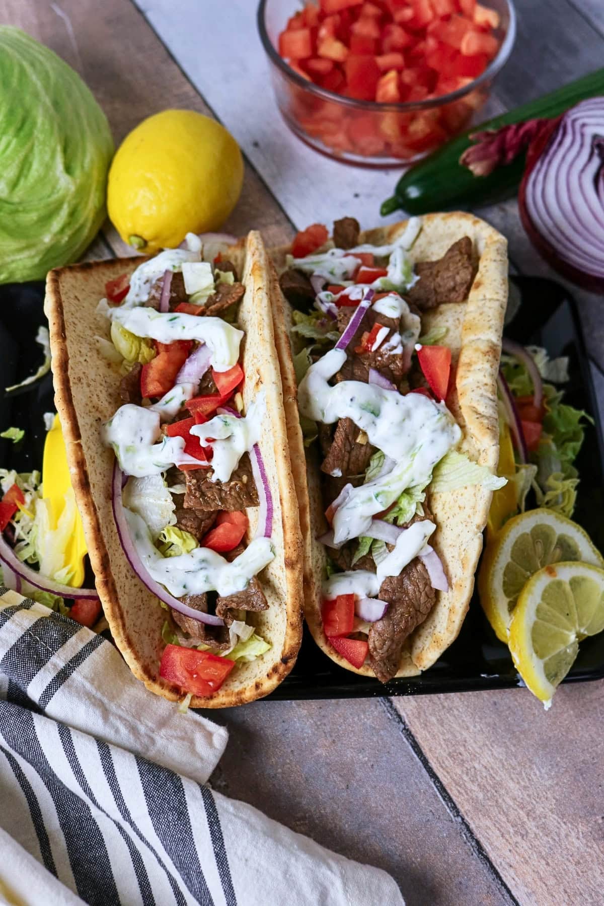 Two gyros with beef, lettuce, tomato, onion, and tzatziki on flatbread.