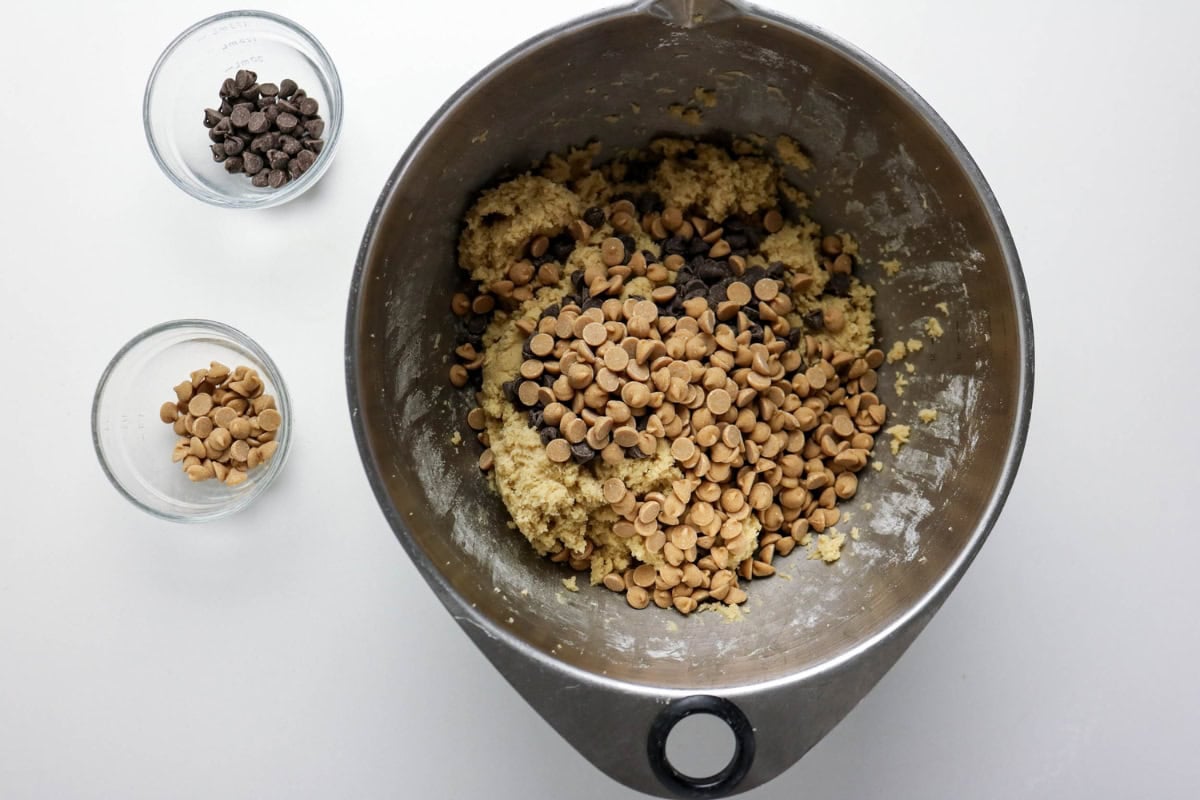 Mixing bowl with cookie dough, chocolate, and peanut butter chips; two small bowls.