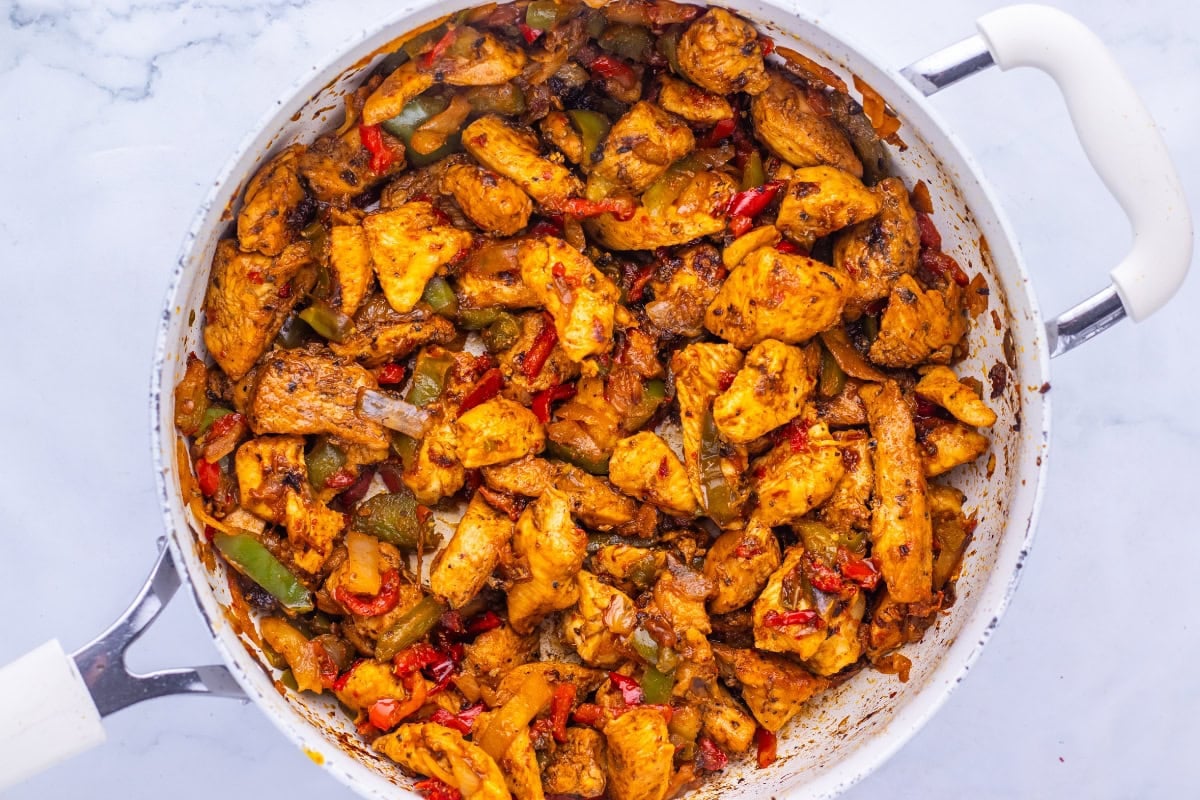 Chicken fajita mix with peppers and onions cooking in a white skillet.