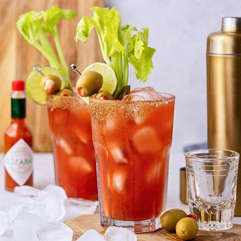 Two Bloody Mary cocktails garnished with celery, olives, and lime on a table.