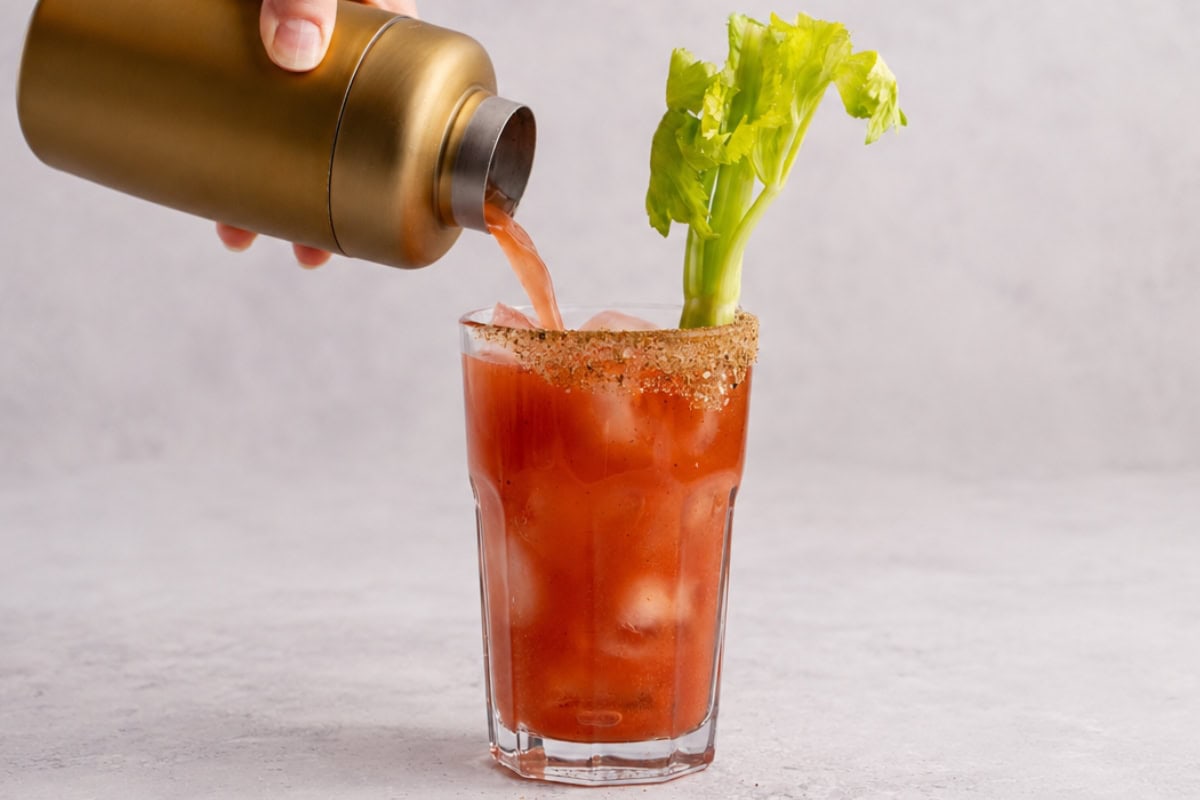 A Bloody Mary cocktail with celery garnish being poured from a shaker.