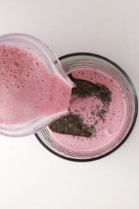Pink smoothie being poured into a glass with chia seeds on top.
