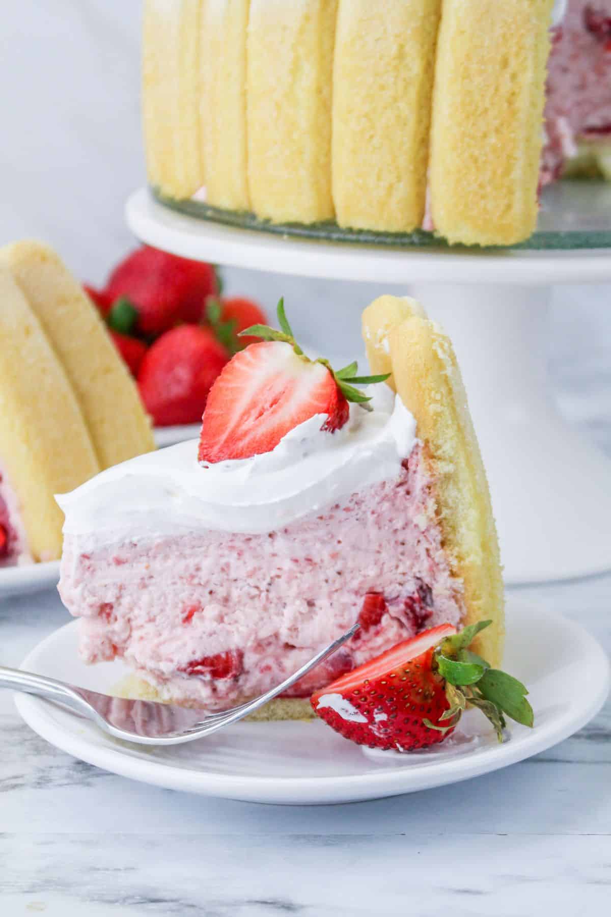 A slice of strawberry charlotte cake with whipped cream and fresh strawberries.