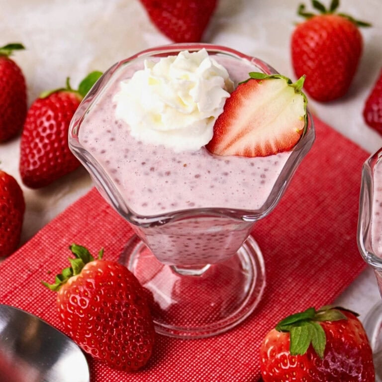 Strawberry chia pudding in a glass, topped with cream and a sliced strawberry.