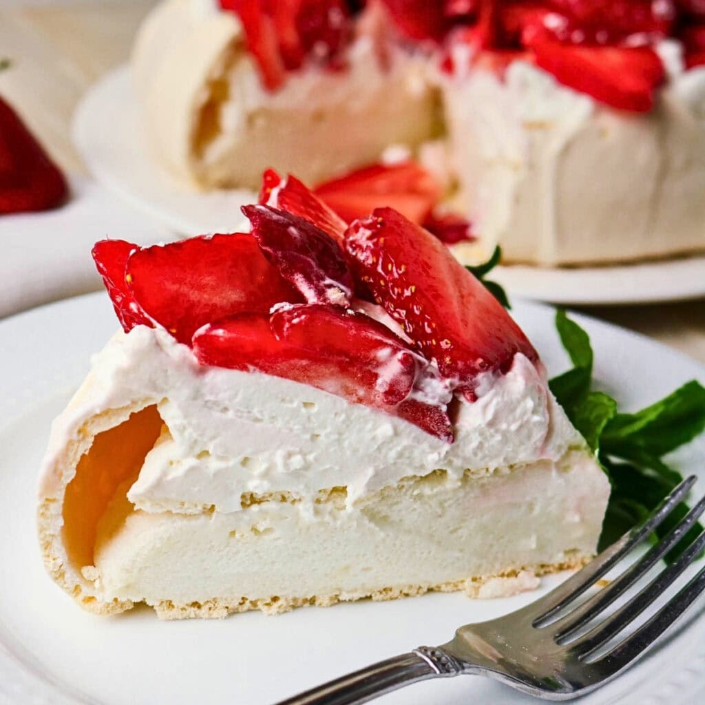 A slice of pavlova topped with whipped cream and fresh strawberries on a plate.