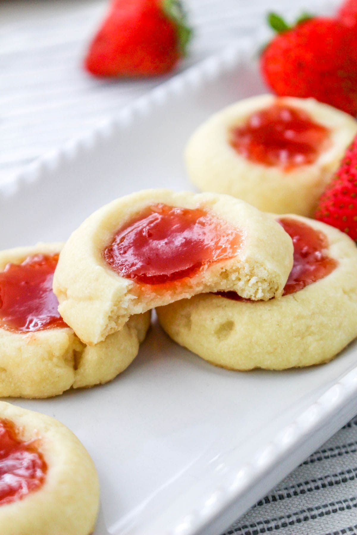 Strawberry jam thumbprint cookies on a white plate, one with a bite taken.