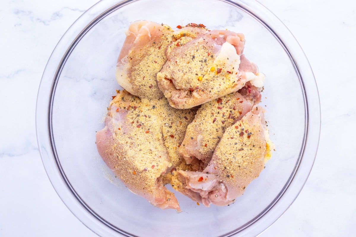 Chicken thighs seasoned in a bowl.