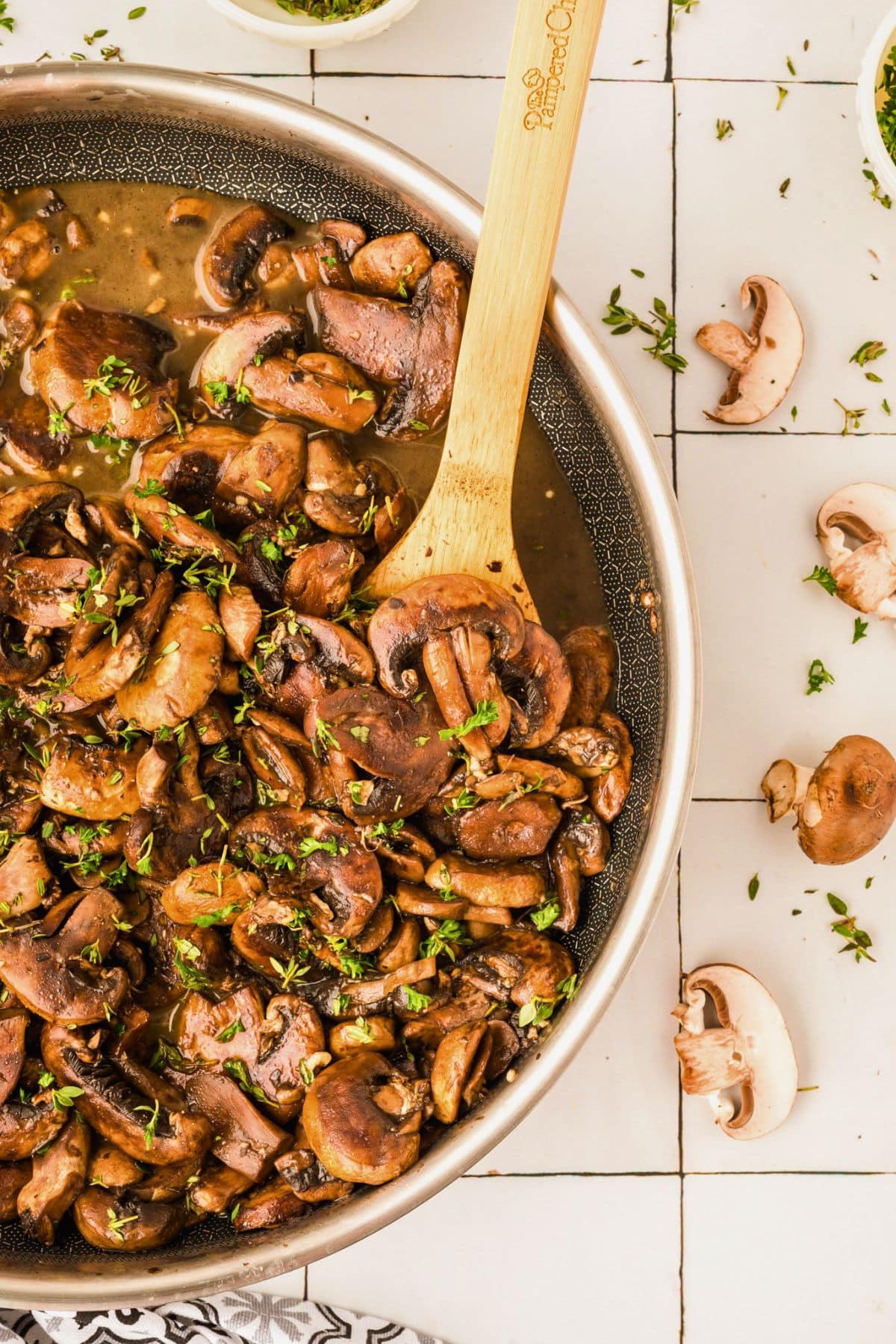Sautéed mushrooms in a pan with fresh herbs, stirred with a wooden spoon.