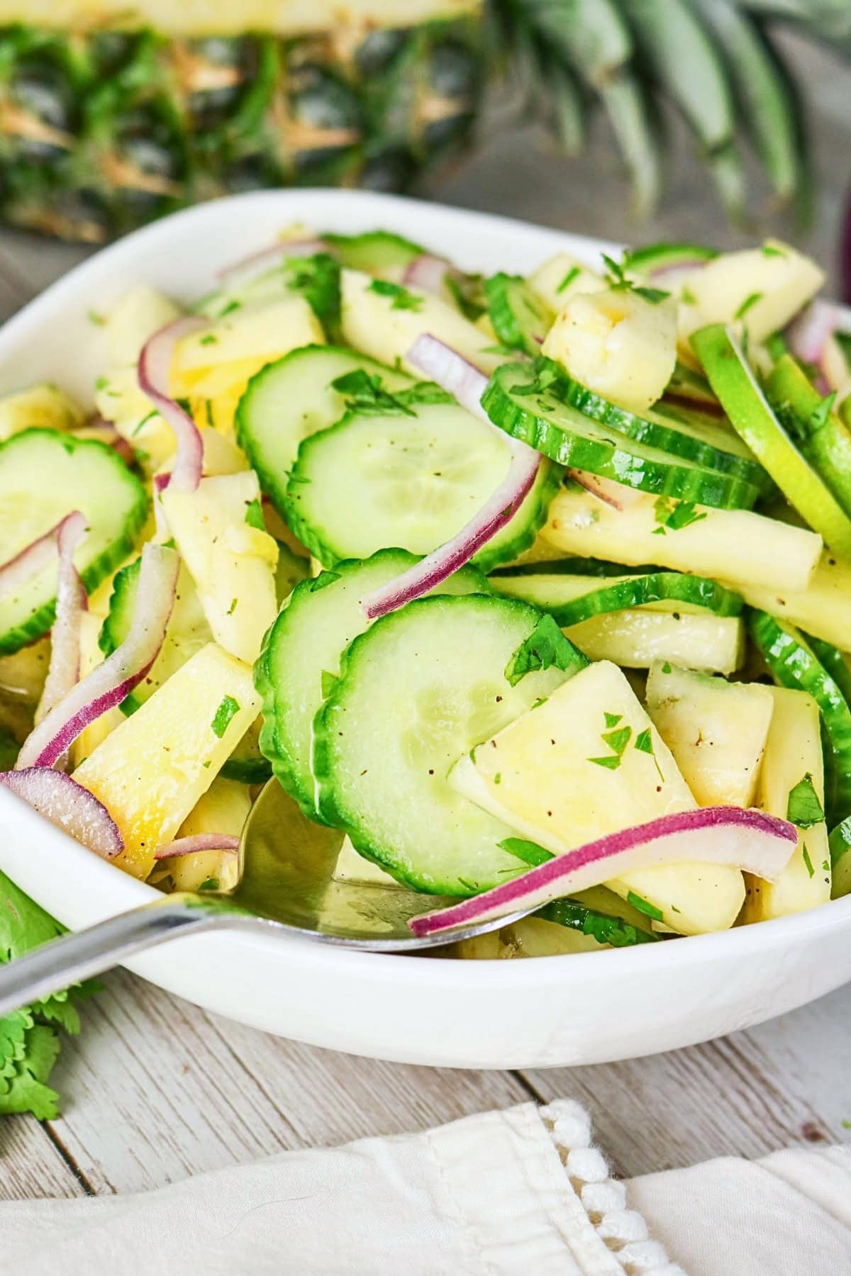 Cucumber, pineapple, red onion, and cilantro salad in a white bowl.