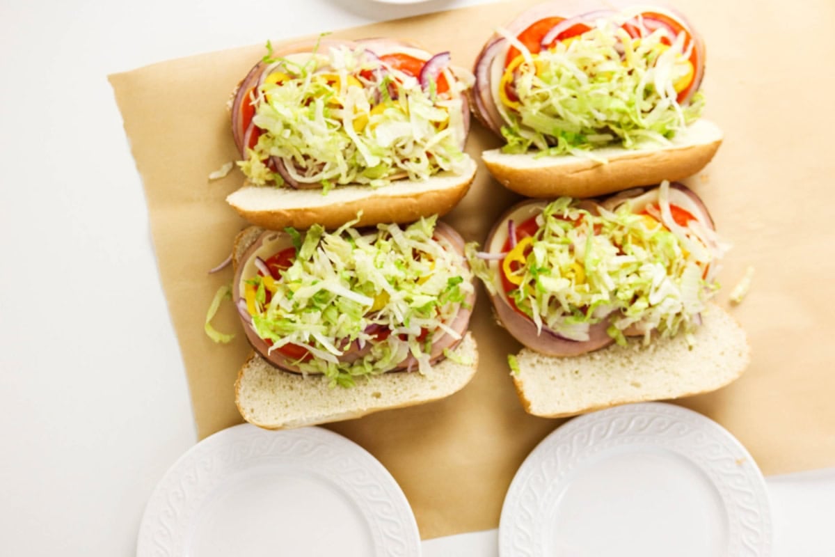 Four hoagie sandwiches filled with lettuce, tomatoes, onions, and deli meat.