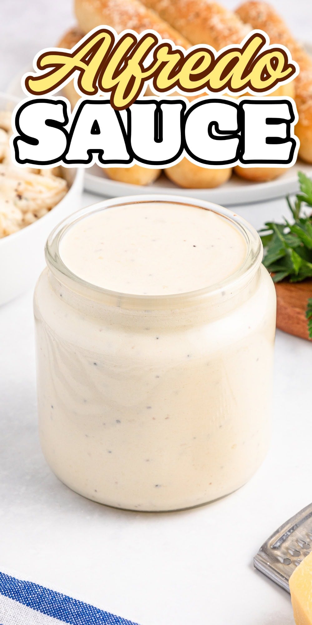 Jar of creamy alfredo sauce on a kitchen counter with garnish nearby.