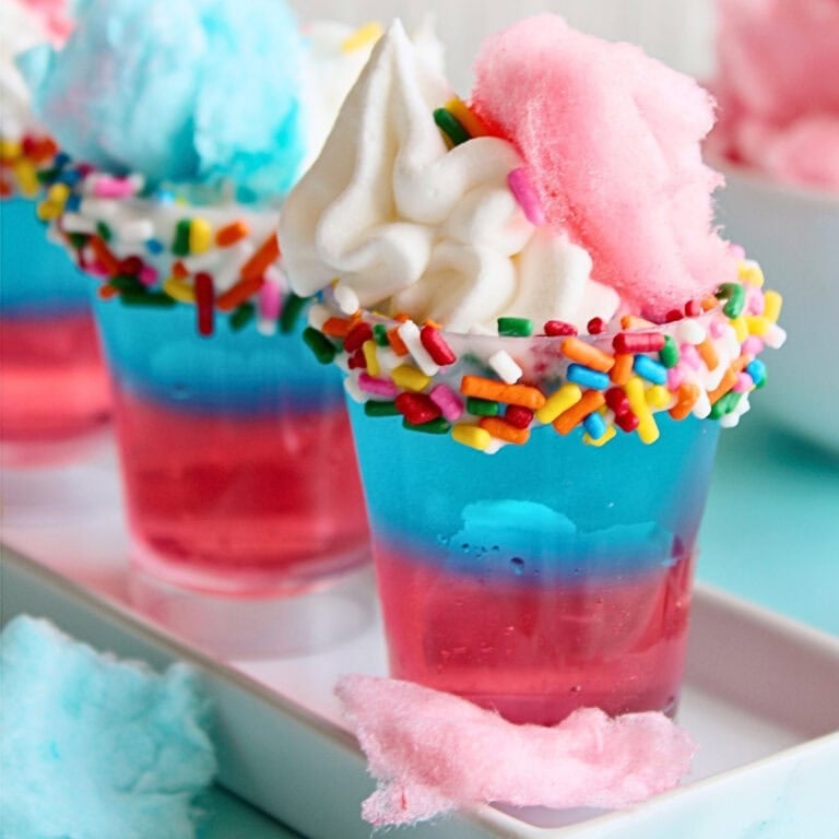 A colorful dessert shot with whipped cream, sprinkles, and cotton candy on top.