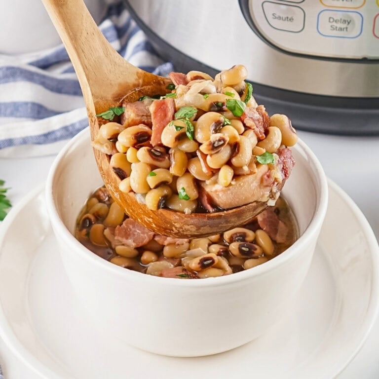 A wooden spoon serves black-eyed peas with ham into a white bowl.
