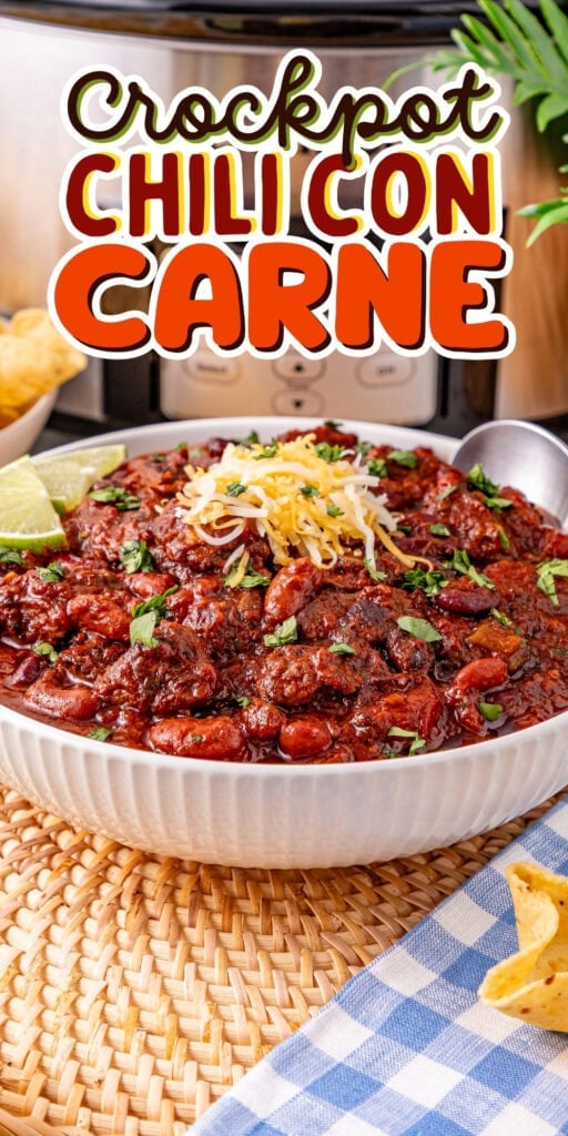 A bowl of chili con carne with cheese and lime, in front of a crockpot.