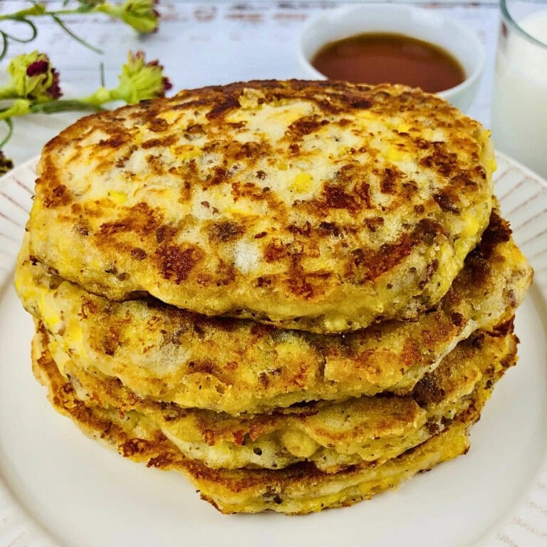 Stack of golden-brown pancakes on a plate, with syrup and milk nearby.
