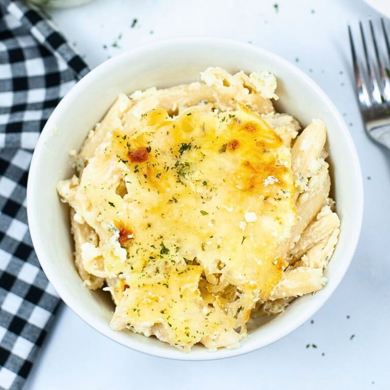 Bowl of baked cheesy pasta with herbs, next to a fork and checkered napkin.