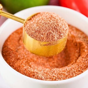A gold spoon scooping tajin seasoning from a white bowl.