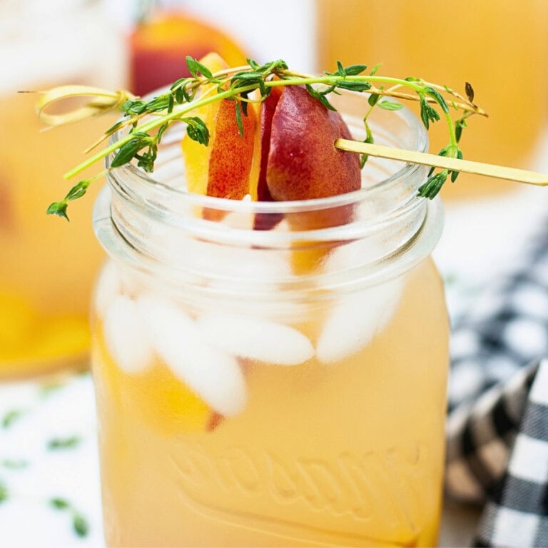 Iced peach drink in a mason jar, garnished with peach slices and thyme.